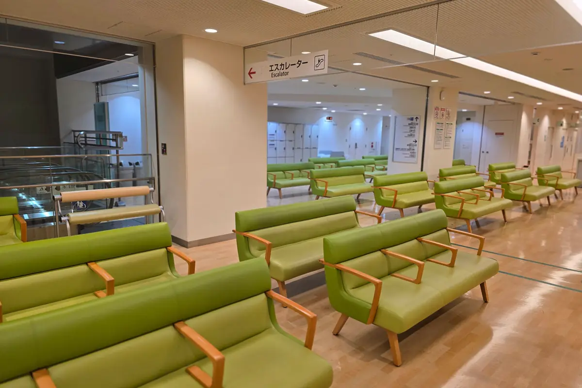 Sala de espera ampla com sofás verdes enfileirados e sinalização no corredor