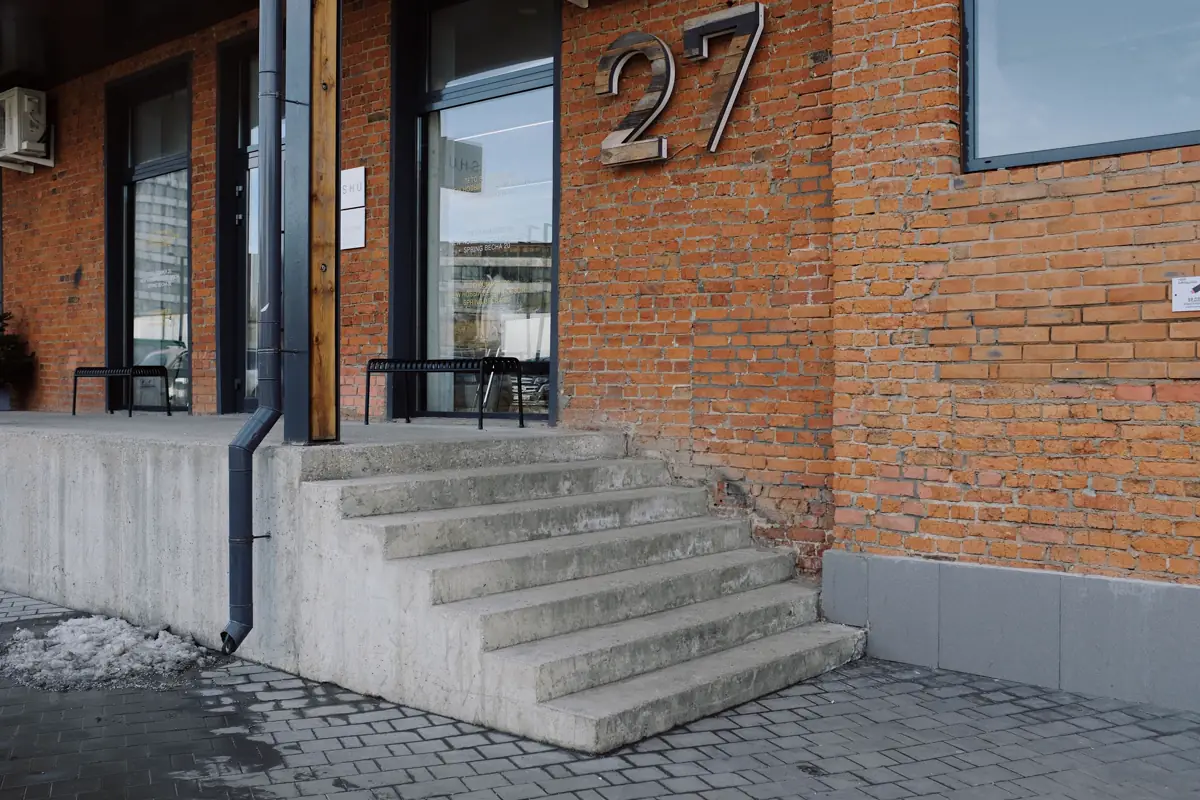 Escada de concreto na entrada de um prédio de tijolos aparentes, sem rampa