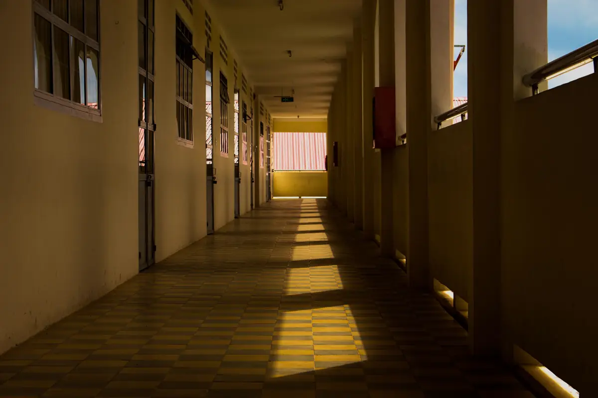 Corredor de escola com portas das salas de um lado e janelas do outro, iluminado pelo sol
