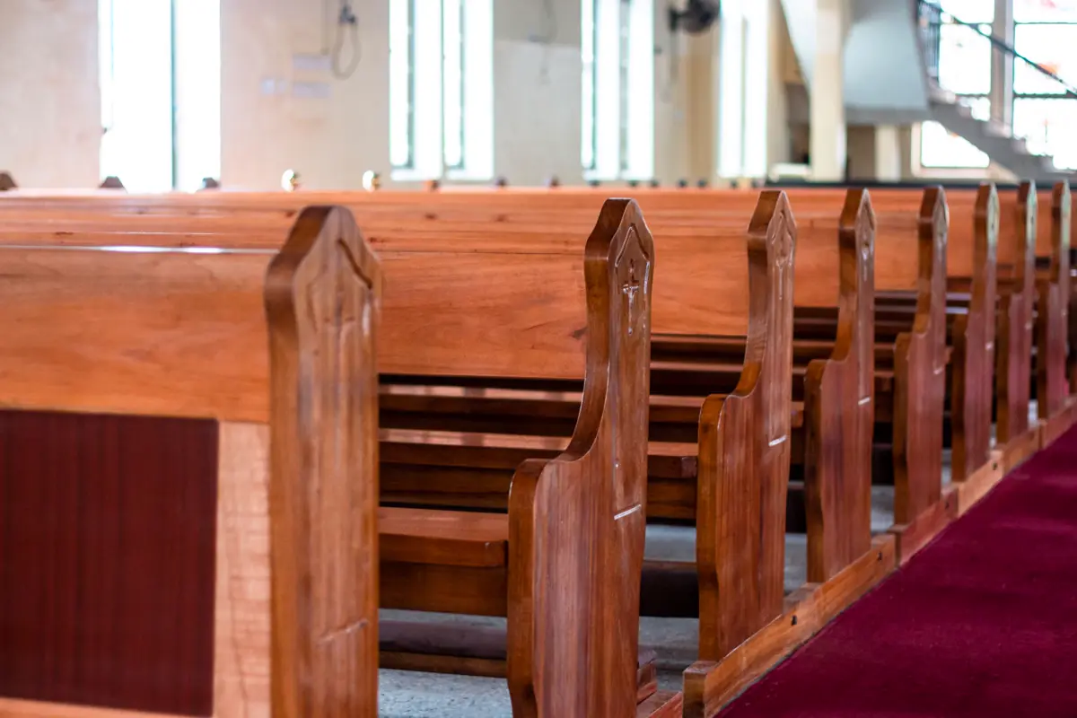 Bancos de madeira enfileirados ao longo do corredor de uma igreja com tapete vermelho