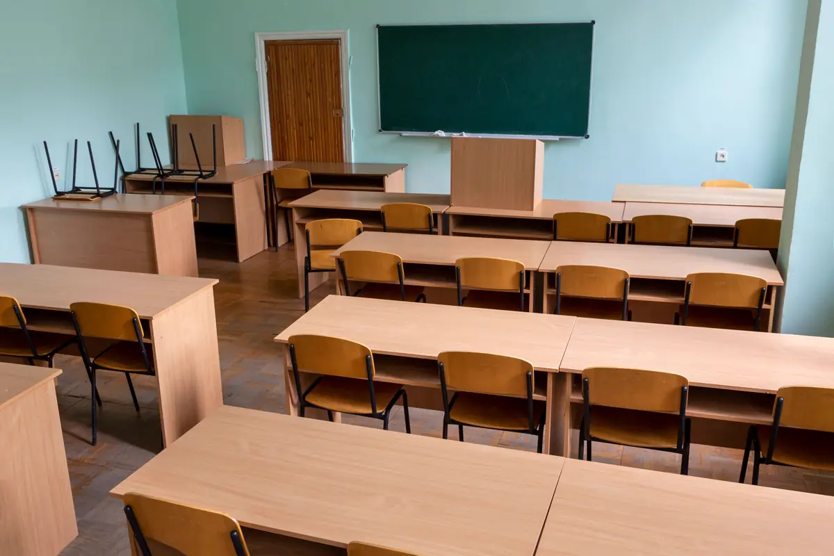 Sala de aula com mesas de madeira, cadeiras e quadro verde na parede