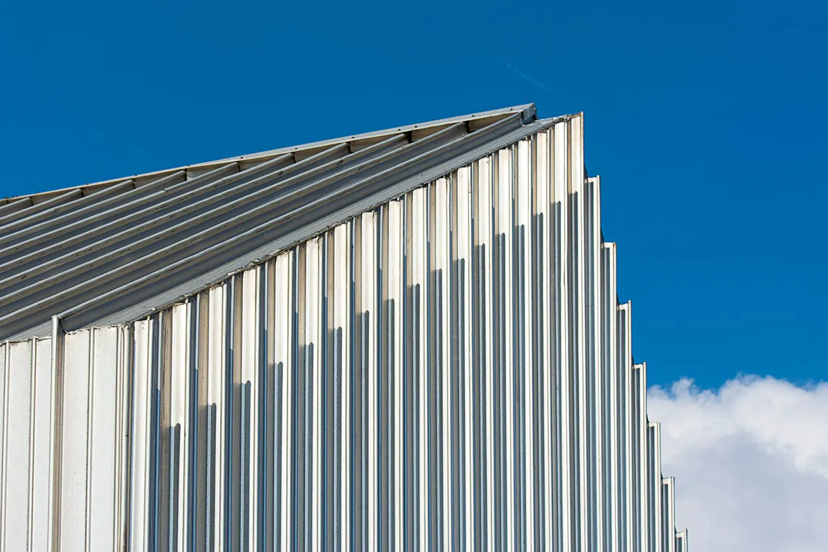 Canto de galpão com fechamento lateral e cobertura em telha metálica trapezoidal prateada contra o céu azul