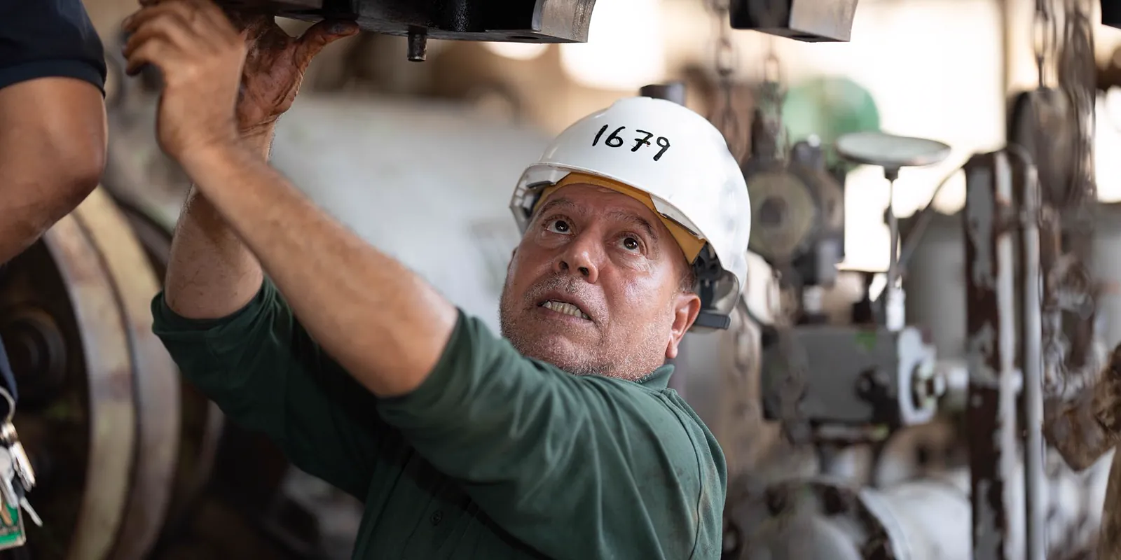 Inspetor com capacete de segurança examinando tubulações e conexões metálicas em planta industrial