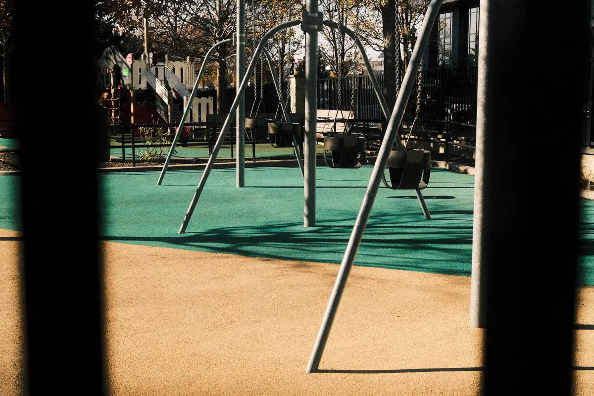 Balanços vazios em playground urbano com estrutura metálica e piso de segurança