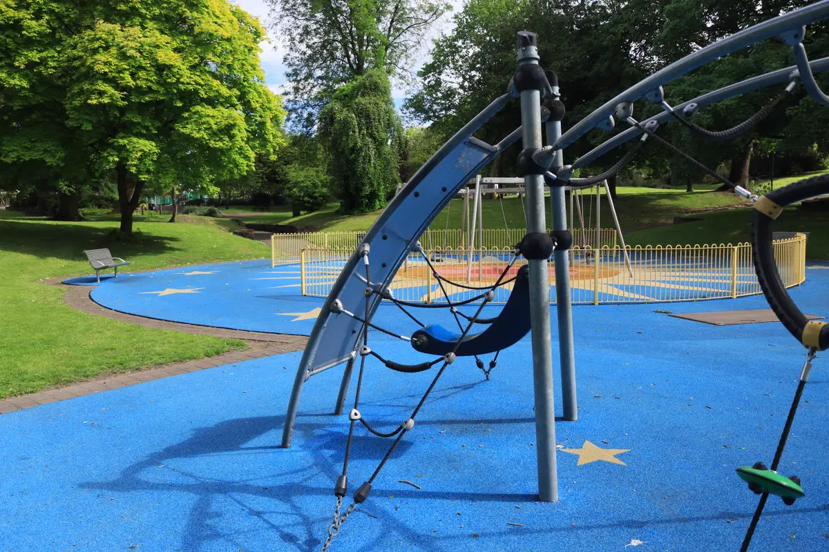 Piso emborrachado azul contínuo em playground, com brinquedo de escalada e área de balanços cercada