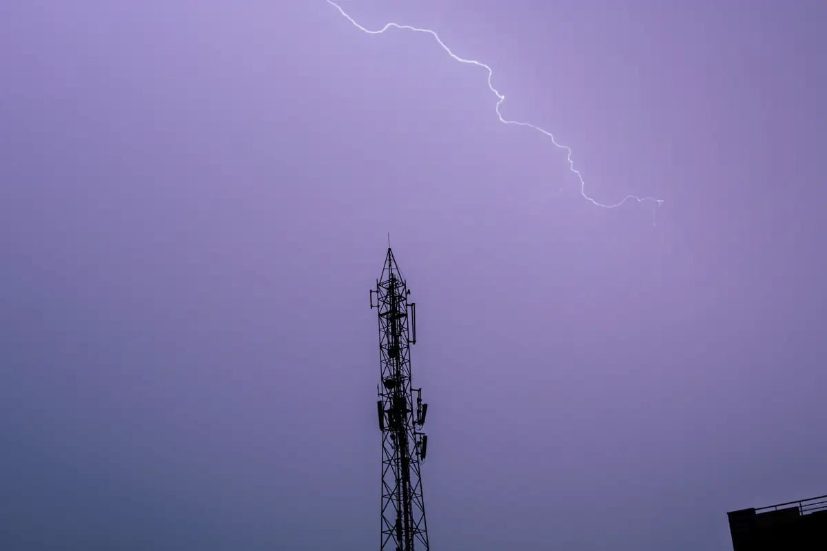 Raio caindo próximo a uma torre metálica de telecomunicações sob céu roxo